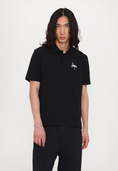 Black polo shirt with a collar, three buttons, and an embroidered pink flamingo logo on the left chest. Short sleeves and smooth texture.