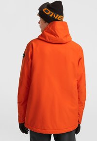 Oranje waterdichte jas met een hoge kraag, verstelbare capuchon en elastische manchetten. Bevat een logo-opdruk op de linkermouw.