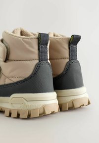 Beige og grå støvler med en blød indvendig foring, velcrorem og strukturerede gummisåler for bedre greb. Har forstærket hæl og ankelstøtte.