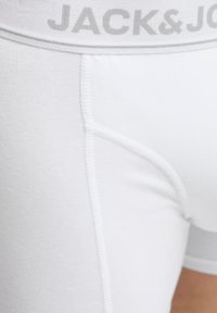 Bijele pamučne bokserice s uzicom u sivoj boji na kojoj je istaknut tekst "JACK & JONES". Glatka tekstura s pojačanim detaljima šivanja.