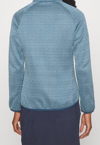 Blue patterned jacket with a diamond texture, featuring long sleeves and a high collar. Accented with a solid blue hem and cuffs.