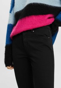 Suéter de mezcla de lana en rayas azul claro, negro y rosa, combinado con jeans negros de corte slim con bolsillos frontales y un sutil detalle de metal.