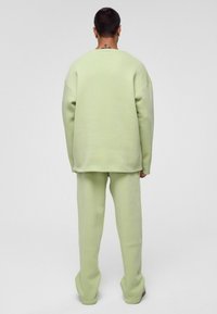 Lichtgroene sweatshirt en bijpassende broek gemaakt van dikke stof. Relaxte pasvorm, verlaagde schouders, met zichtbare stikseldetails.