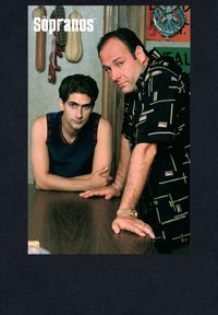 Due uomini si appoggiano a un tavolo di legno. Uno indossa una canotta blu, l'altro una camicia nera con un motivo. Sullo sfondo ci sono decorazioni per le pareti.