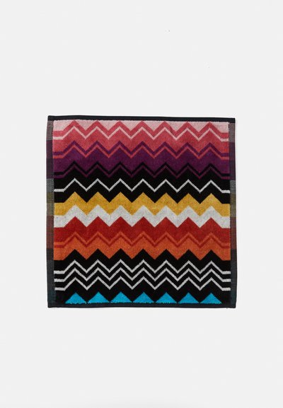 Multicolored rectangular rug featuring zigzag patterns in shades of pink, orange, black, and blue. Made of textured fabric with a bordered edge.