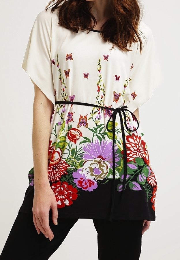 Tunique florale en crème et noir, arborant des motifs de fleurs et de papillons vibrants. Fabriquée en tissu doux avec une taille ceinturée pour plus de définition.