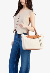 Borsa a spalla intrecciata beige con dettagli in pelle marrone e manici intrecciati. Presenta una chiusura con zip e un'etichetta che recita "Sono una borsa responsabile."