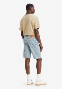 Light blue denim shorts with a relaxed fit, featuring a brown leather patch at the back waist. Paired with a beige short-sleeve shirt.
