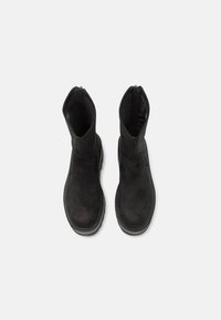 Botines negros de ante, con textura suave, punta redonda y cremalleras laterales. La suela es gruesa y ligeramente texturizada.