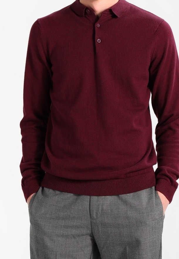 Burgunderfarbener Strickpullover mit Henley-Kragen, drei Knöpfen, gerippten Bündchen und Saum, kombiniert mit grauen karierten Hosen.