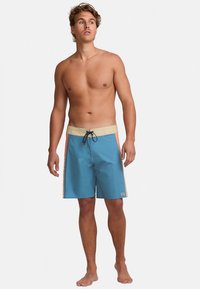 Mėlynos spalvos maudymosi šortai su smėlio spalvos juosmeniu ir oranžiniais šonų akcentais. Yra raištelis ir prekės ženklas apatinėje kairėje pusėje.