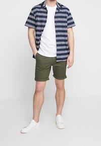 Koszula z krótkim rękawem w kolorze granatowym z białymi geometrycznymi paskami, w połączeniu z oliwkowymi, podwiniętymi szortami i białymi trampkami. Prosty, casualowy design.