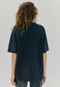 Černé oversized tričko s volným střihem, kulatým výstřihem a krátkými rukávy, se mírně vybledlou texturou a měkkou tkaninou.