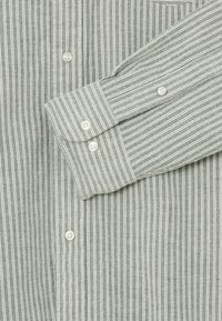 Grün-weißer, vertikal gestreifter Button-Down-Hemd mit langen Ärmeln und weißen Knöpfen an den Manschetten und dem Frontverschluss.