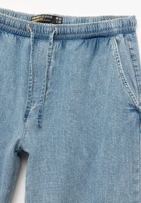 Helle blaue Jeans-Jogginghosen mit elastischem Bund, Kordelzug, Seitentaschen und Etikett mit der Größe W32 L32 sowie "Jogger Fit."