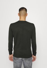 Maglione lungo verde scuro con maniche lunghe, scollatura arrotondata, polsini e orlo a costine, texture morbida e design aderente.