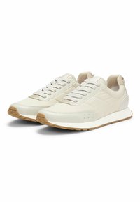 Zapatillas de cuero blancas con detalles en gris claro, paneles laterales texturizados y suela de goma. Presentan cordones redondos y detalle del logotipo en el lateral.