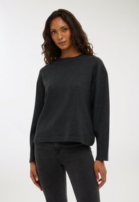 Czarny sweter z dzianiny z okrągłym dekoltem, luźnym krojem i długimi rękawami. Miękka tekstura i gładkie wykończenie. Noszony z ciemnoszarymi dżinsami.