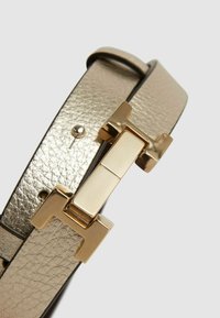 Metallisk guld läderbälte med en rektangulär guldspänne och texturerad yta, med enhetlig bredd och justerbara hål.