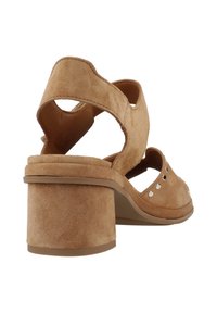 Sandali con tacco in suede beige, con tacco a blocco, punta aperta e lati ritagliati. Decorati con piccoli rivetti argentati lungo il bordo superiore.