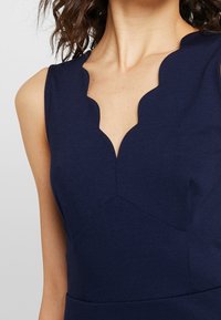 Marinblå ärmlös klänning med en scalloped halsringning och mjuk textur, med geometriska sömmar och figurnära silhuett.