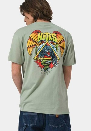 Camisa de algodón verde claro con un vibrante diseño gráfico en la parte posterior que presenta un pantera, alas, garras y texto en negrita en varios colores.