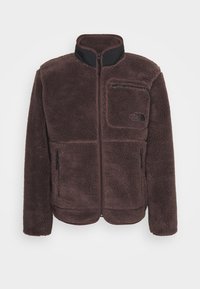 Brun fleecetröja med hög krage, blixtlåsstängning och två blixtlåsfickor på sidan. Har en liten bröstficka och texturerad tyg.