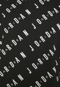 T-shirt nera con un motivo di testo bianco ripetuto che scrive "JORDAN" in varie orientazioni e dimensioni su tutta la stoffa.