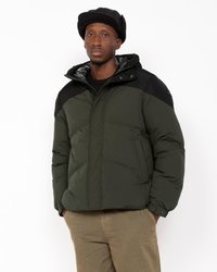 Casaco tipo puffer em verde escuro com detalhes em preto. Apresenta capuz, fecho de correr e bolsos laterais. Feito de material isolante com acabamento texturizado.