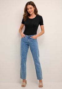 Schwarzes, geripptes Kurzarmshirt kombiniert mit hellblauen, gerade geschnittenen Jeans und beigen Sandalen mit Blockabsatz. Glatte Texturen, figurbetontes Design.