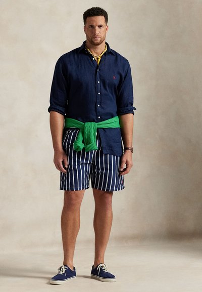 Nakitljiva mornarska lanena košulja na kopčanje, prugaste mornarske kratke hlače, zelena pletiva majica vezana u struku, plave platnene cipele, nošene uz žutu bandanu.