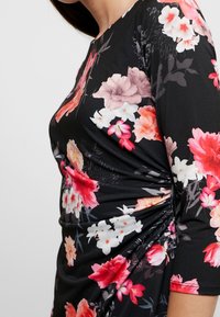 Bloemige jurk met een zwarte achtergrond en roze en witte bloemen, geraffineerde zijdetails en driekwartmouwen. Zacht, rekbaar materiaal.