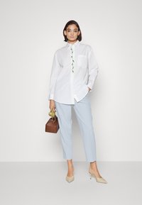 White button-up shirt with floral embroidery, paired with light blue trousers. Beige heels and a brown handbag complete the look.