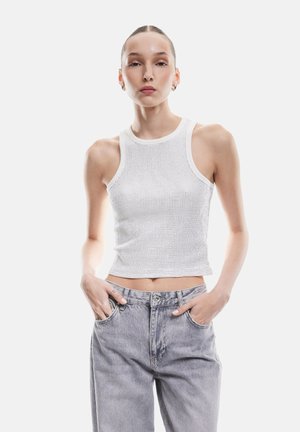 Top corto de punto blanco con textura acanalada, combinado con jeans de tiro alto gris claro, que cuentan con bolsillos frontales y un corte relajado.