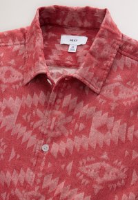 Camicia rossa con motivi e colletto, caratterizzata da un design tribale in tonalità più chiare. Realizzata in tessuto con chiusura a bottoni e etichetta interna.