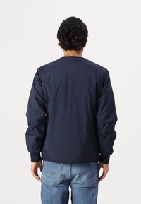 Veste bleu marine en tissu léger et lisse. Présente des poignets côtelés et un col rond. La vue montre l'arrière sans matériel visible.