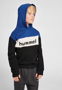 Bluza z kapturem w niebieskie, czarne i białe bloki kolorystyczne, z logiem "hummel". Materiał jest miękki, teksturowany, z ściągaczami przy mankietach i u dołu.