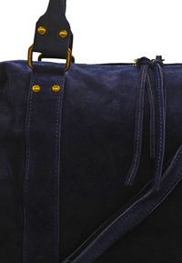 Sac en suede bleu marine avec quincaillerie dorée, bandoulière ajustable et détails avec nœuds. Texture douce, design minimaliste et lignes épurées.