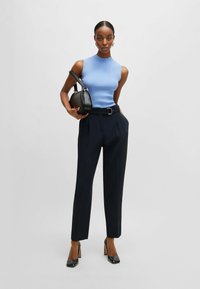 Top smanicato a coste blu chiaro abbinato a pantaloni navy a vita alta, dotati di una cintura. Borsa nera e scarpe con tacco completano l'outfit.