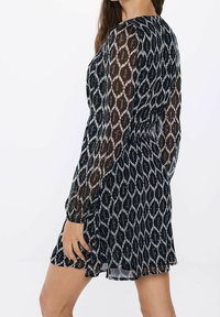 Robe à motifs noir et blanc avec manches longues, taille cintrée et jupe évasée. En tissu léger et transparent avec des dessins géométriques.