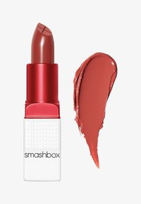 Rouge à lèvres Smashbox dans un tube rouge avec une étiquette blanche, présentant un échantillon de couleur mauve lisse et crémeux à côté.