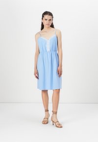 Light blue dress with lace trim and adjustable spaghetti straps, gathered waistline, and knee-length skirt. Paired with strappy brown heels.