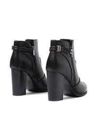 Stivaletti neri in pelle sintetica con punta arrotondata, zip laterale e tacco alto impilato. Presentano doppi fibbie e una texture liscia.