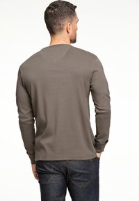 Olijfgroene lange mouwen shirt met een ronde hals, geribbelde textuur en gestikte afwerking bij de halslijn, gedragen met donkere jeans.