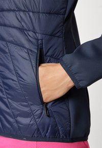 Navy puffer jacket with quilted texture and side zip pocket. Features a smooth fabric finish and a fitted design with elastic cuffs.