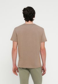 Καφέ κοντομάνικη μπλούζα από μαλακό, λείο ύφασμα. Διαθέτει στρογγυλή λαιμόκοψη και απλό σχέδιο με εφαρμοστή γραμμή, παρουσιάζοντας την πίσω όψη.