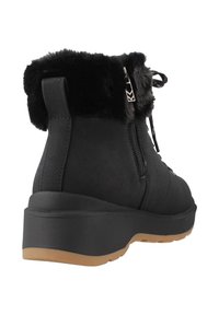 Botas negras de tobillo con puño de pelaje sintético, cierre de cremallera y suela de goma texturizada. Presentan una construcción sólida y una suela exterior marrón en contraste.