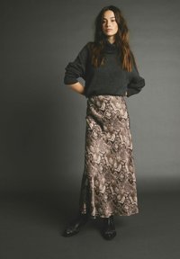 Sort oversized turtleneck sweater parret med en gulvlang satin nederdel med slangeprint i nuancer af beige og brunt, akkompagneret af sorte hælede støvler.