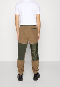 Brown and green patchwork pants with a soft texture, featuring a fitted waistband and a rear pocket with a blue accent.