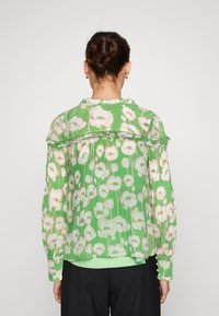 Transparante, groene blouse met een bloempatroon in wit en roze, met een gerimpelde kraag en lange mouwen, geplooide textuur en een ontspannen pasvorm.